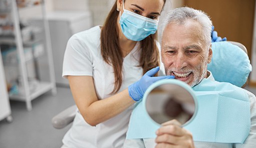 An aging gentleman admiring his new dental implants with a hand mirror