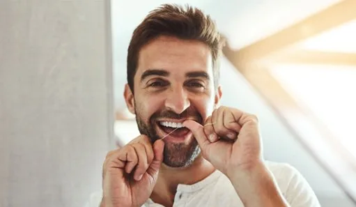 Man smiling while flossing his teeth in bathroom