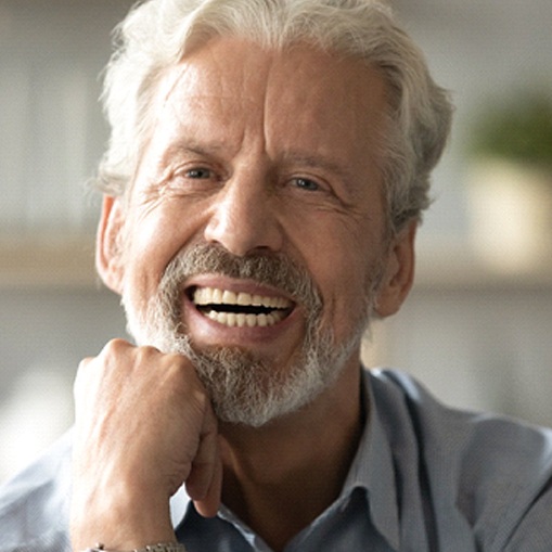 An older gentleman propping his head with his hand and showing off his new dentures in Oshkosh