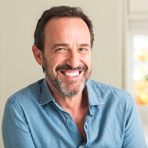 An older man wearing a blue button-down shirt and smiling after learning he is a qualified candidate for dentures