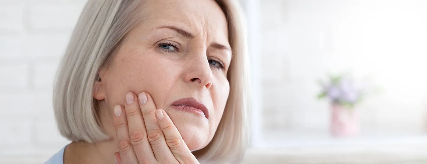 Woman sitting on couch with tooth pain needing emergency dentist in Oshkosh, WI