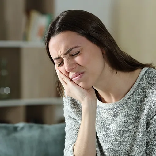 Woman in grey shirt rubbing jaw in pain