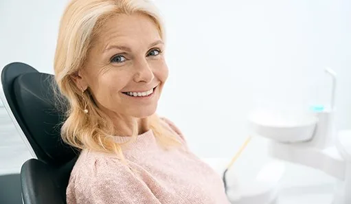 Woman in pink shirt sitting in dental chair and smiling