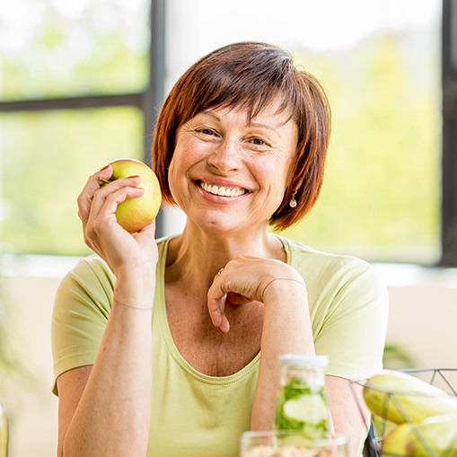 Smiling woman eating an apple after dental implant tooth replacement