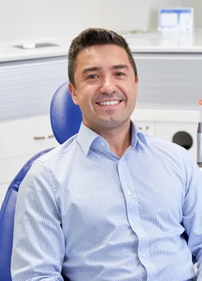 Man in a pale blue collared shirt smiling while sitting in dental chair