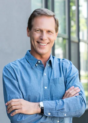 Man in a blue button up shirt smiling with his arms crossed