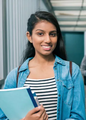 Teenage girl with a backpack holding books in a hallway