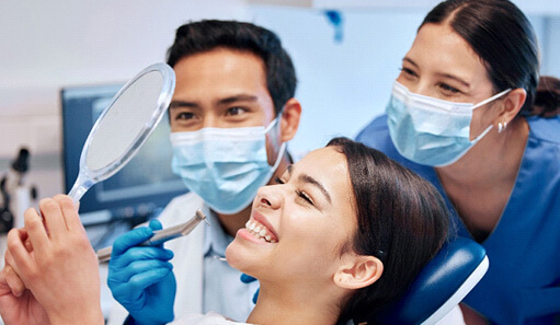 patient looking at smile in mirror with dentist and dental hygienist