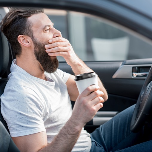 Exhausted man yawning and drinking coffee while driving