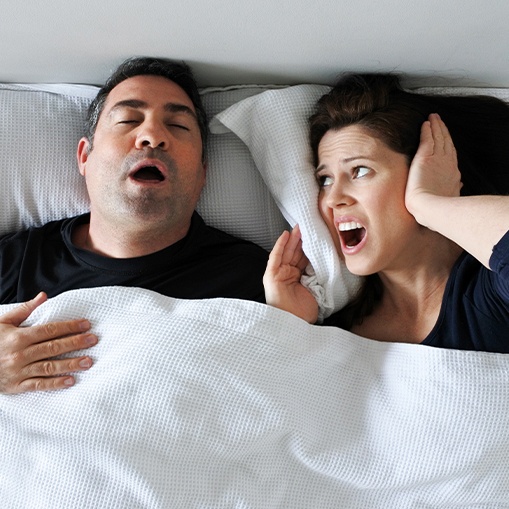 Frustrated woman covering her ears next to snoring man
