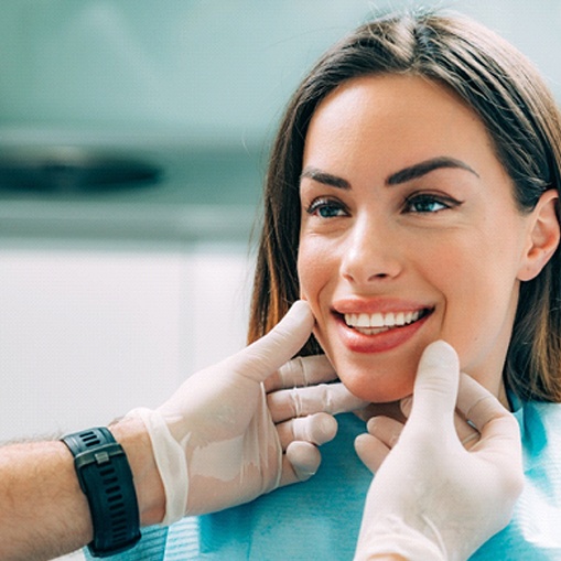 A young woman smiling while her dentist examines her teeth after receiving veneers in Oshkosh