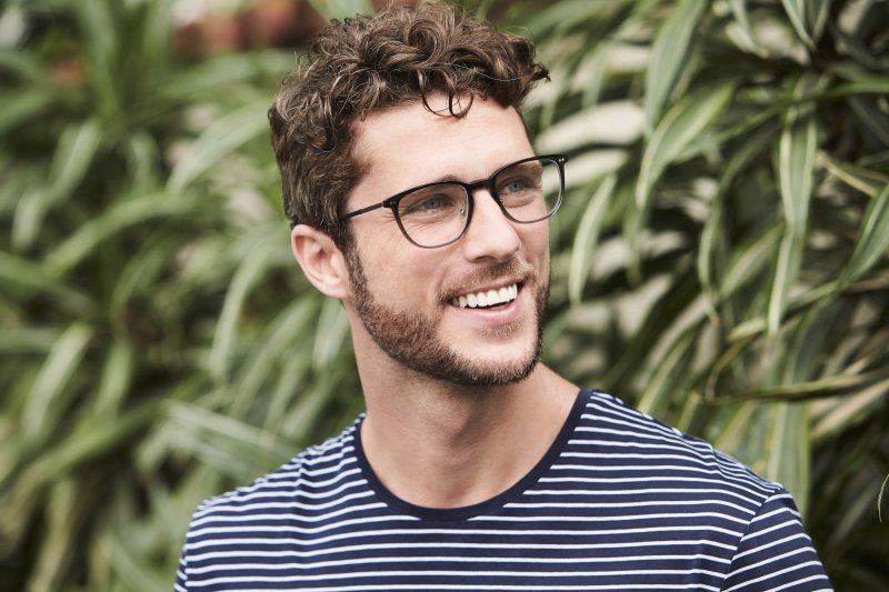 a young man wearing a striped shirt and glasses shows off his brighter smile after undergoing teeth whitening in Oshkosh 