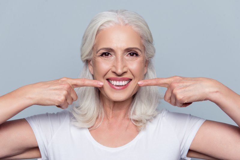 Senior smiling and pointing to their teeth